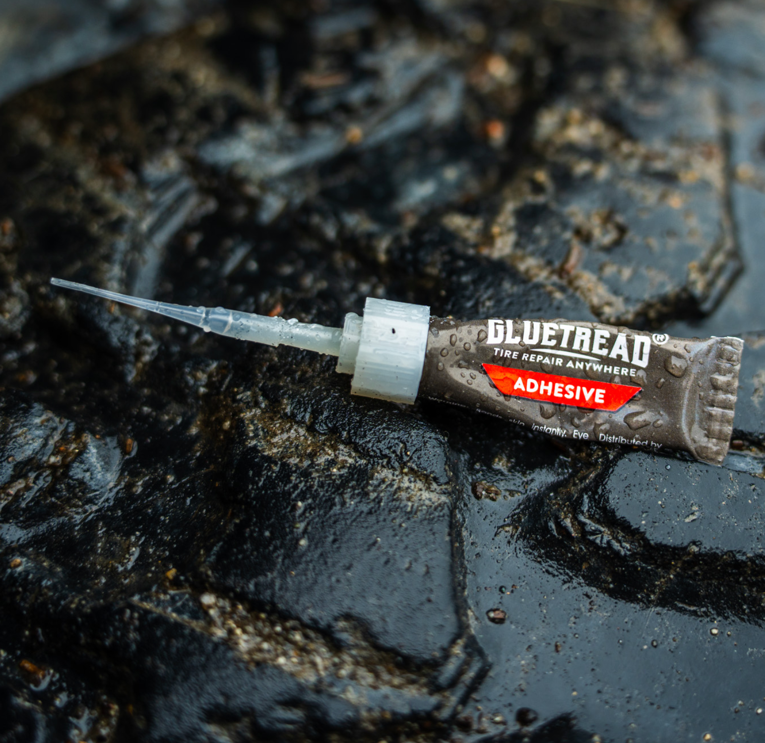 GlueTread tire repair adhesive tube with applicator tip on a wet off-road tire
