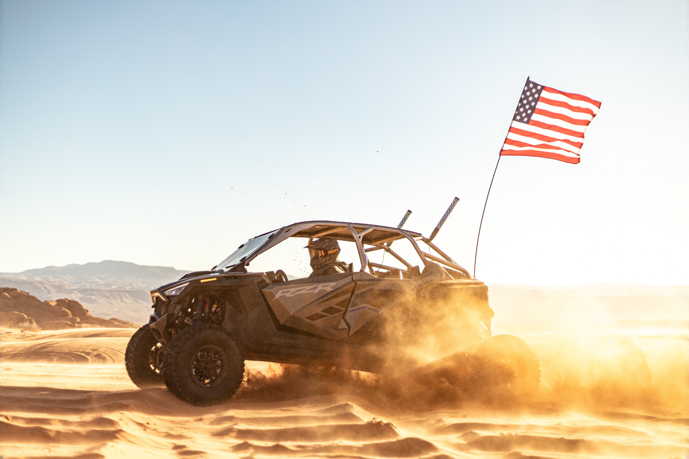 Off-road vehicle driving through desert terrain with an American flag attached